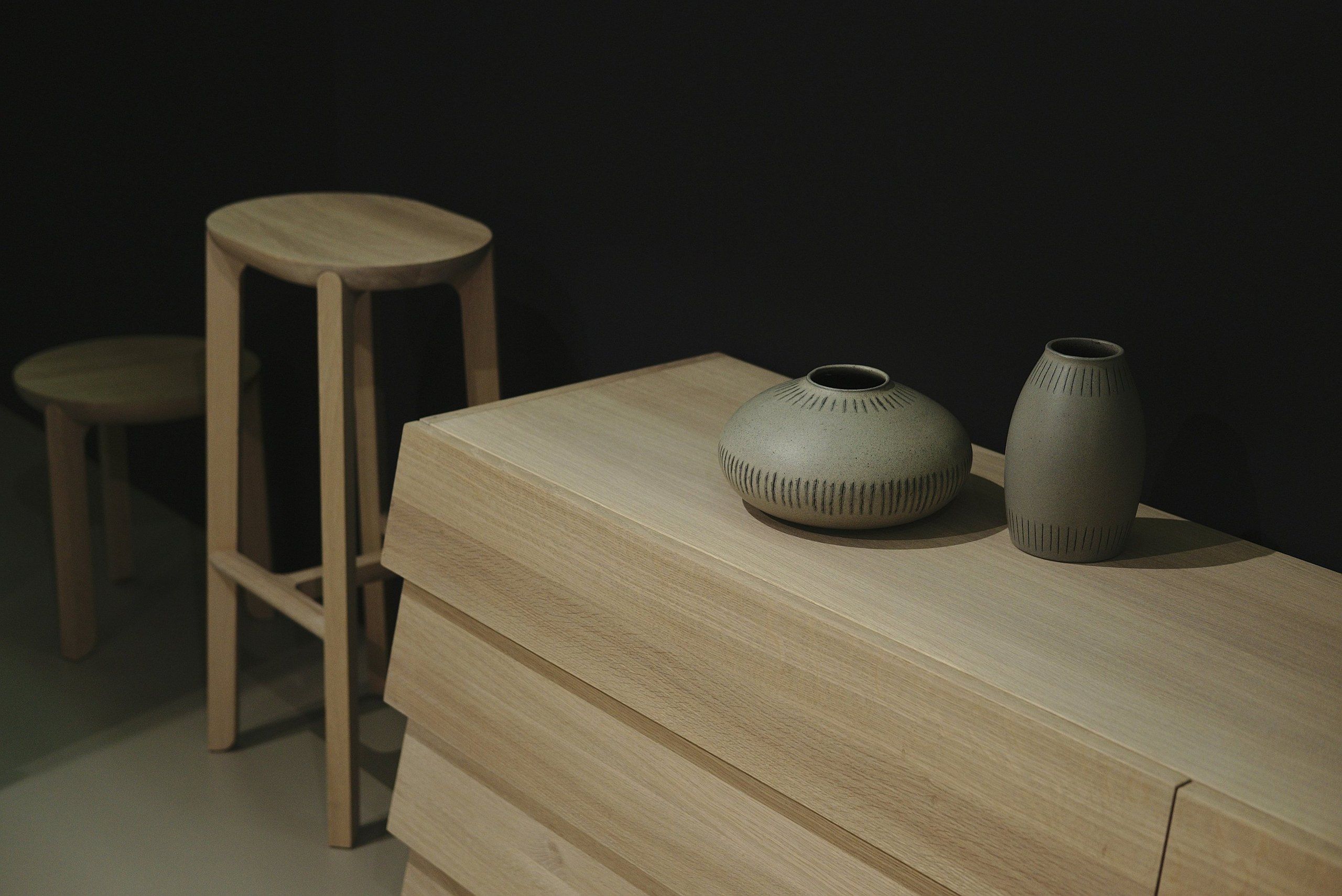 Oak sideboard with two ceramic vases and timber stools in a dark room