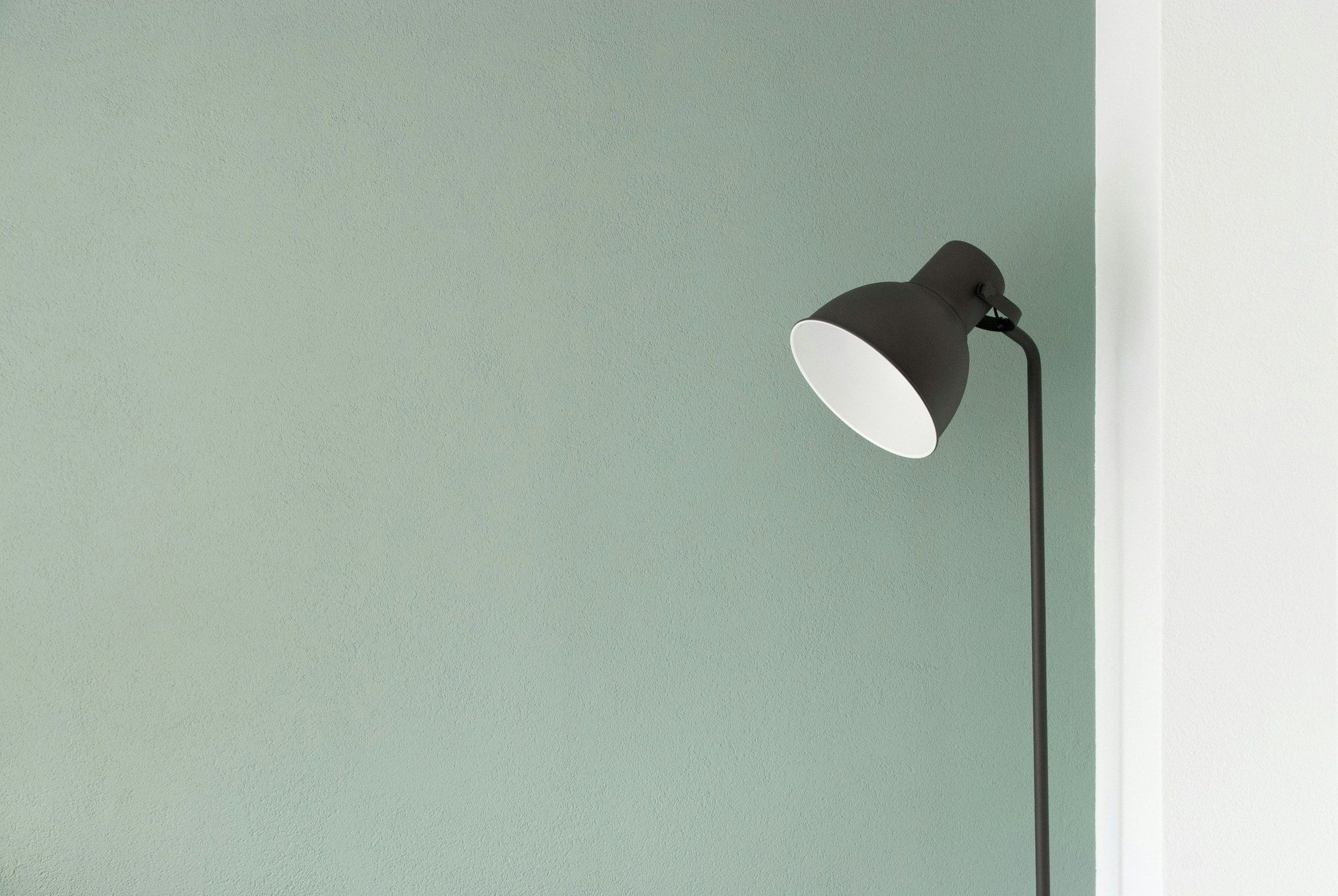 Black floor lamp against a sage green wall